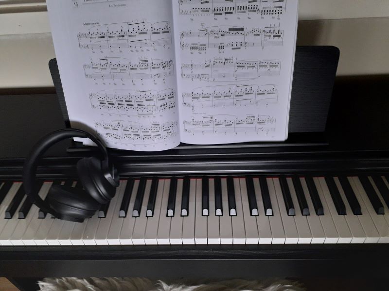 Picture of black electonic piano, with headphones and sheet music